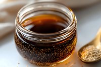 Golden honey in glass jar with sparkling bubbles and wooden spoon on light background, macro food photography showing natural sweetener texture.