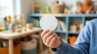 Child holding blank white circle card in playroom with toys and shelves, suitable for educational materials, advertising, and creative projects.