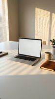 Modern laptop with blank white screen on clean desk workspace with morning sunlight streaming through window blinds creating warm shadows and peaceful atmosphere.