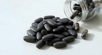 Black oval pills and capsules spilled from glass bottle on white background for pharmaceutical and healthcare supplement concepts.