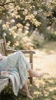 Woman in floral skirt relaxing barefoot on wooden garden bench with tea cup, surrounded by blooming spring trees in soft sunlight.