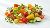 Fresh colorful vegetable medley with zucchini, bell peppers, cherry tomatoes and herbs on white background for healthy cooking and meal preparation.
