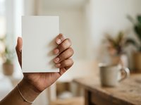 Close-up of hand holding blank white card in bright interior space with potted plants, suitable for branding, marketing mockups, and business presentations.