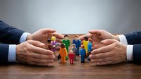 Businessman hands protecting diverse colorful figurines on wooden surface, representing employee care, team protection, and human resources management concept.