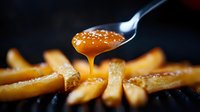 Dripping salted caramel sauce from spoon onto golden french fries creates sweet and savory fusion cuisine moment on dark background. Perfect for food marketing.
