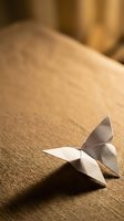 Delicate paper origami butterfly resting on textured fabric surface with warm golden lighting creating soft shadows and peaceful zen atmosphere.