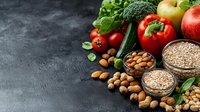 Fresh organic produce, nuts and grains arranged on dark concrete background. Raw ingredients including vegetables, fruits, almonds and oats for healthy eating and cooking.