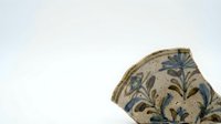 Young woman with light skin tone wearing a decorative ceramic vessel fragment featuring blue botanical motifs on neutral background, isolated for design and educational use.