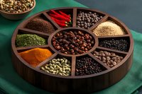 Aromatic spices and seasonings in wooden compartment box on green textile background, including peppercorns, chili, cardamom, turmeric and dried herbs.
