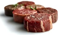 Four raw beef tenderloin medallions with sea salt and rosemary, isolated on white background. Fresh premium cuts ready for grilling or cooking.