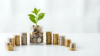 Financial growth concept with green plant sprouting from coins in glass jar surrounded by stacked money representing investment and savings success.