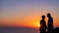 Romantic couple silhouettes holding hands watching sunset over ocean horizon creating intimate moment during golden hour for love and relationship concepts.