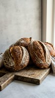 Freshly baked artisan sourdough bread loaves with decorative scoring on rustic wooden cutting board in modern kitchen setting for bakery and food photography.