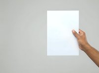 Hand holding blank white paper sheet against neutral gray background for mockup and branding presentations.
