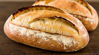 Fresh baked artisan sourdough bread loaves with golden crust and flour dusting on rustic wooden table for bakery and homemade cooking concepts.