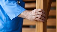 Senior male worker in blue uniform holding wooden beam on construction site or carpentry workshop.
