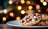 Fresh baked cranberry and white chocolate chip cookies on white plate with festive bokeh lights background creating cozy holiday atmosphere.