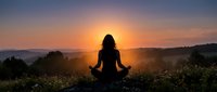 Woman silhouette meditating in lotus pose during golden sunset over mountain landscape. Peaceful yoga practice outdoors for wellness and mindfulness concept.