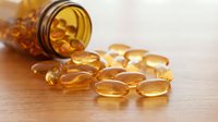 Omega-3 fish oil capsules spilling from amber glass bottle on wooden surface for health and wellness supplement photography.