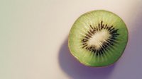 Fresh kiwi fruit half showing green flesh and black seeds on neutral background for healthy eating and nutrition concepts.