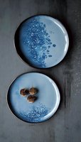 Artisanal ceramic plates in soft blue glaze with organic bubble pattern and dried figs, set against dark textured background for food photography and menu design.