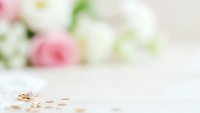 Elegant gold wedding rings with diamond on white surface with soft pink roses in blurred background, romantic bridal jewelry for engagement and marriage ceremony.