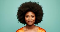 Young African American woman with voluminous natural afro hairstyle wearing orange shirt against turquoise background, suitable for portrait and diversity stock use.