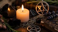 Mystical witchcraft altar with burning candle, pentagram symbols, dried herbs, crystals and ancient spell books for occult rituals and spiritual practices.