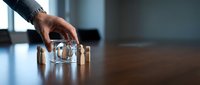 Business professional hand reaching for transparent glass award trophy on wooden desk in modern office environment.