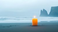 Glowing orange candle on dark beach with misty ocean and dramatic rock formations in background. Serene coastal meditation scene.