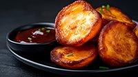 Golden crispy roasted potato slices with herbs served on dark plate with dipping sauce for restaurant menu and cooking blog content.