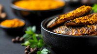 Grilled chicken breast with golden turmeric spice coating in black bowl, garnished with fresh herbs and aromatic spices for healthy cooking and meal preparation.