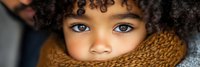 Young mixed-race child with curly hair wearing cozy brown knit scarf, close-up portrait with bright blue eyes for winter fashion and lifestyle concepts.
