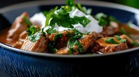 Tender beef chunks in rich brown sauce garnished with fresh parsley and sour cream, served in dark blue ceramic bowl. Traditional meat stew close up.