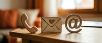 Wooden contact icons phone envelope email symbol on desk in warm office setting for business communication and customer service concepts.