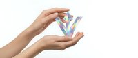 Female hands holding holographic crystal prism with rainbow light refraction on white background, isolated for design projects and creative concepts.