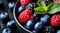 Mixed berries including raspberries, blueberries and blackberries in dark bowl with fresh mint leaves, ideal for food and beverage design projects.