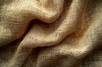 Natural burlap fabric with wavy folds creating abstract texture pattern in warm brown tones, close-up view showing detailed woven structure.