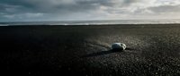 Solitary white shell casting long shadow on dark sand beach with moody overcast sky, suitable for coastal, minimalist, and nature-themed designs.