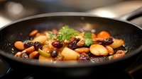 Fresh mixed nuts and dried fruits sautéed in black pan with herbs and spices, close up view of healthy vegetarian cooking process on dark background.