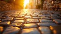 Sunlit cobblestone street at golden hour with dramatic low angle perspective showing textured stones glowing in warm evening light, creating atmospheric urban scene.