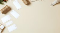 Flat lay overhead view of holiday gift wrapping supplies including twine, blank gift tags, and ribbon on neutral beige background for seasonal packaging projects.