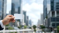 Businessman holding blank white business card with modern city skyline in background for corporate branding and networking purposes.