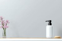 Minimalist bathroom shelf with white ceramic soap dispenser, wooden brush, and pink flowers in glass vase against light gray wall, modern home decor styling.