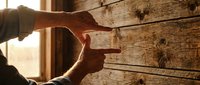 Carpenter hands framing wooden construction project with natural sunlight streaming through window creating warm workshop atmosphere for building renovation.