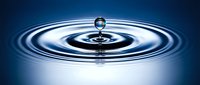 Water drop creating ripples on calm blue surface with concentric circles spreading outward in slow motion photography capturing fluid dynamics and splash effect.