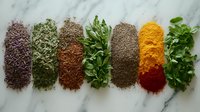 Colorful array of ground spices and fresh herbs arranged in neat rows on marble surface, including turmeric, paprika, dried herbs and fresh parsley leaves.