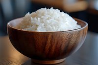 Steamed white jasmine rice served in wooden bowl on dark table, close-up view showing fluffy texture and individual grains in natural lighting.