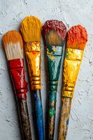 Used paintbrushes with colorful paint stains arranged on textured light background. Artistic tools showing wear and creative process in warm orange and red tones.