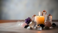 Healing crystals arrangement with burning candle, amethyst cluster and clear quartz points on wooden surface for meditation and spiritual wellness practices.